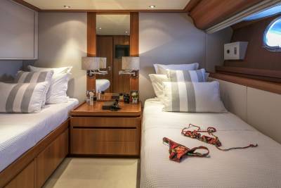 Two twin beds with striped pillows and a bikini lie on a yacht's cozy cabin.