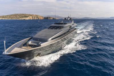 A sleek, modern yacht cruises through the deep blue sea, leaving a white wake against a backdrop of rugged, sun-drenched islands.
