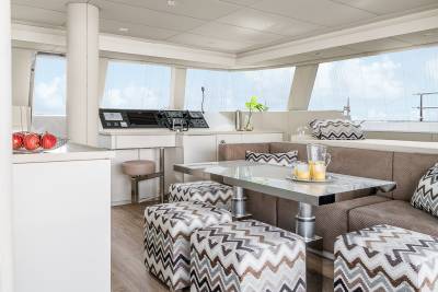 A modern yacht interior features a sleek dining area with a glass-topped table, plush seating, and panoramic windows overlooking the ocean.