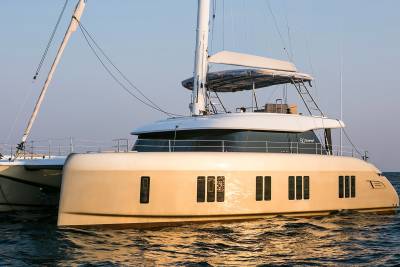 A sleek, modern catamaran glides across calm waters under a clear sky, its golden hull reflecting the warm sunlight.