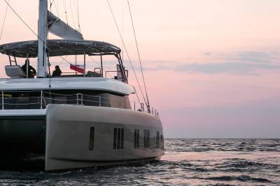 A sleek catamaran glides through calm waters under a soft, pastel sky at dusk.
