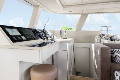 The modern yacht interior features a sleek helm station with advanced navigation screens and comfortable seating overlooking the bright blue sky.