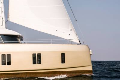 A sleek, modern catamaran glides through the deep blue water under a vast, pale sky.