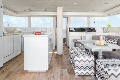 A modern yacht interior features a sleek white kitchen and a dining area with patterned seating.
