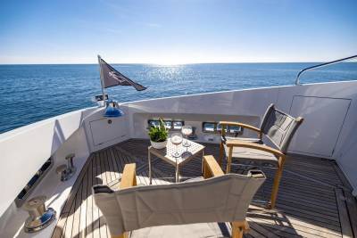 Two chairs and drinks await on the deck of a yacht, overlooking a tranquil blue sea under a clear sky.