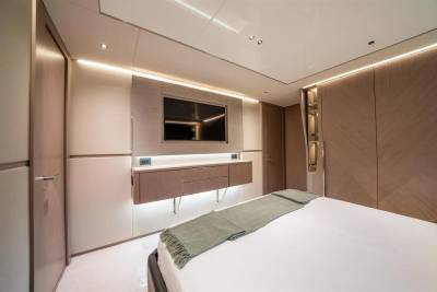 Luxurious yacht cabin features a wall-mounted television, sleek cabinetry, and a comfortable bed adorned with a green throw.