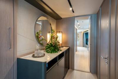 A sleek entryway features a round mirror, decorative floral arrangement, and a glimpse into a well-lit corridor.