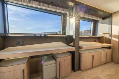 Sunlight streams through the windows of this luxurious yacht cabin, illuminating the elegant wooden cabinetry and offering a breathtaking view of the rocky coastline.