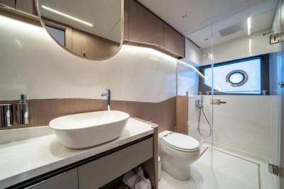 A sleek, modern yacht bathroom features a vessel sink, contemporary toilet, and a glass-enclosed shower with a porthole window.