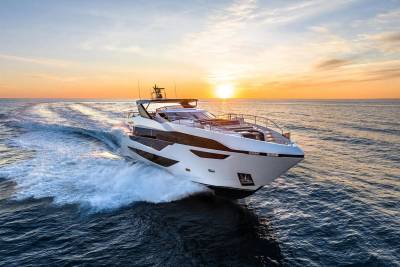 A sleek white yacht cuts through the deep blue ocean at sunset, leaving a trail of white foam in its wake.
