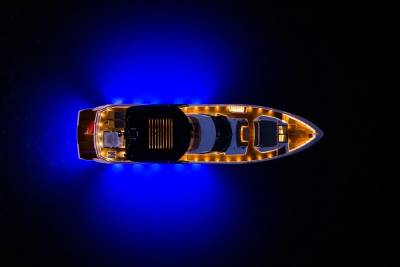 A luxurious yacht glows with warm interior lights and vibrant blue underwater illumination against the dark night sea.