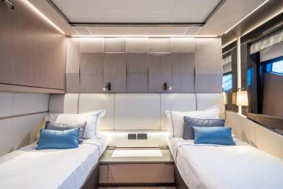 Luxurious twin beds in a modern yacht cabin are adorned with plush blue and grey pillows.
