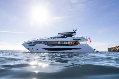 A sleek white yacht glides through shimmering blue waters under a bright, sunlit sky.