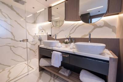 A modern yacht bathroom features dual vessel sinks, a glass-enclosed shower, and elegant marble-patterned walls illuminated by soft lighting.