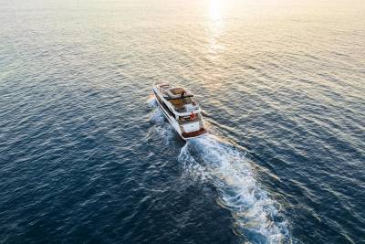 A luxurious yacht glides through the calm ocean waters, leaving a white wake in its path as the sun sets.