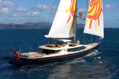 The majestic yacht Clara glides through azure waters, its vibrant sails catching the sun's rays against a backdrop of lush islands.