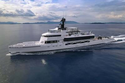 The luxurious yacht Wanderlust glides through calm blue waters with a mountainous coastline in the distance.