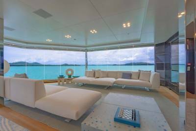 Luxurious white sofas face panoramic windows overlooking turquoise waters and lush green islands under a cloudy sky.
