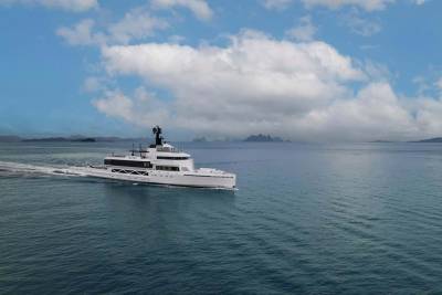 A sleek white superyacht cruises through calm turquoise waters under a dramatic sky.