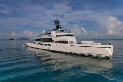 A sleek white superyacht named Wanderlust glides through calm turquoise waters near a cluster of tropical islands.