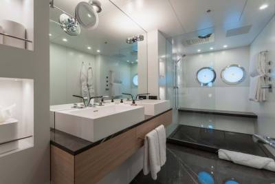 Modern yacht bathroom features dual vessel sinks, a sleek glass-enclosed shower, and illuminated porthole windows.