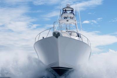 A powerful white yacht cuts through the ocean waves under a bright blue sky with fluffy clouds.
