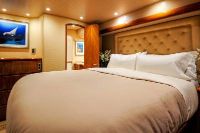A luxurious yacht bedroom features a large bed with plush pillows, a tufted headboard, and a framed ocean-themed artwork.