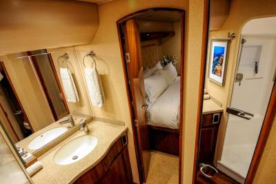 Luxurious yacht interiors feature a well-appointed bathroom with dual sinks and a glimpse into a cozy stateroom.