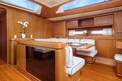 A luxurious yacht dining area features warm wood paneling, comfortable seating, and elegant place settings under a skylight.