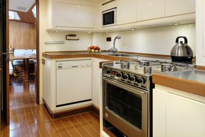 A compact galley kitchen features a stainless steel oven and stovetop, a dishwasher, and a kettle, all set against warm wood accents.