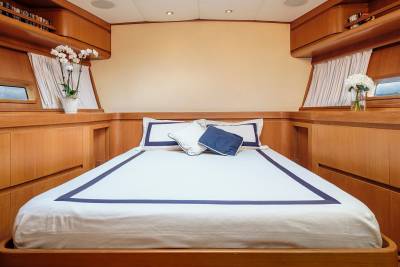 A luxurious yacht cabin features a neatly made bed with crisp white linens and blue trim, flanked by warm wood paneling.