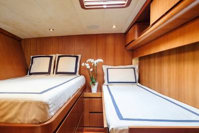 Luxurious wooden paneling surrounds two neatly made beds, one double and one single, adorned with crisp white linens and navy trim.