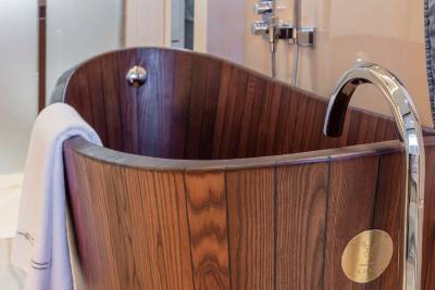 A luxurious wooden bathtub with a sleek chrome faucet offers a serene bathing experience.