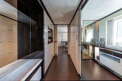 A luxurious yacht hallway features polished wood floors, sleek cabinetry, and reflective surfaces creating an elegant and spacious ambiance.