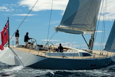 A majestic yacht sails through the ocean under a bright blue sky with billowing sails and a Union Jack flag.