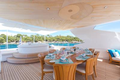 A beautifully set dining table awaits guests on the deck of a yacht, overlooking a serene coastal landscape.