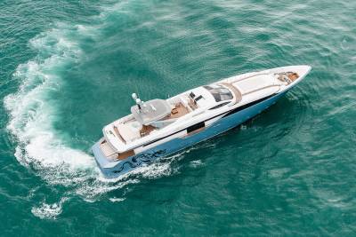 A sleek blue and white yacht glides through turquoise waters, leaving a foamy wake in its path.