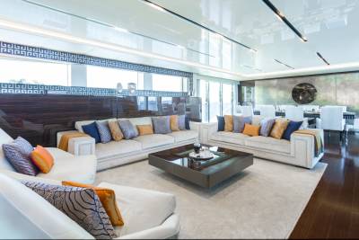 Luxurious yacht salon features plush white sofas, geometric patterned pillows, and a sleek coffee table overlooking the ocean.
