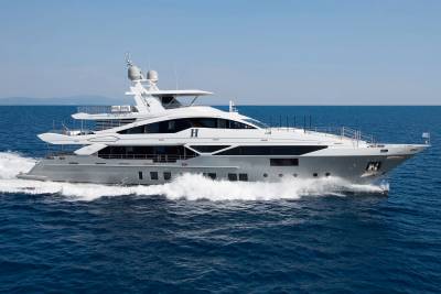 A large, luxurious white yacht is speeding across the calm, blue waters of the ocean, with mountains visible in the distant background.