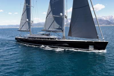 A sleek black yacht with dark sails glides through the deep blue sea under a bright sky.