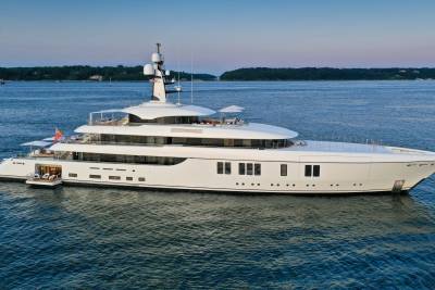 A luxurious white superyacht glides serenely on calm blue waters under a twilight sky.