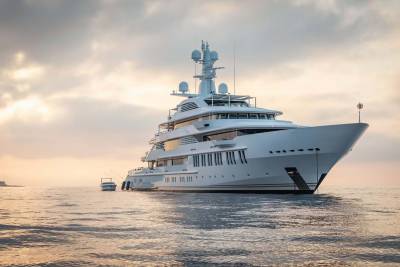A magnificent white superyacht floats serenely on calm waters under a soft, golden sky.