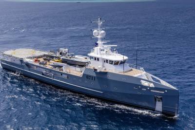 A sleek grey vessel with a helipad and tenders cruises through the deep blue ocean.