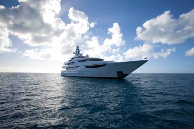 A luxurious superyacht glides through the deep blue ocean under a dramatic sky filled with fluffy white clouds.