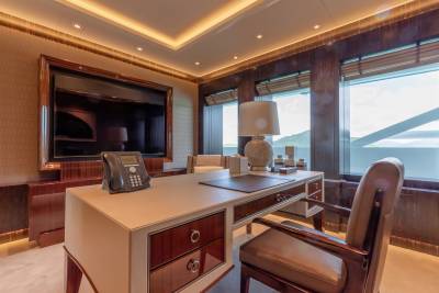 A luxurious yacht office features a large desk, a comfortable leather chair, and a stunning view of rolling green hills.