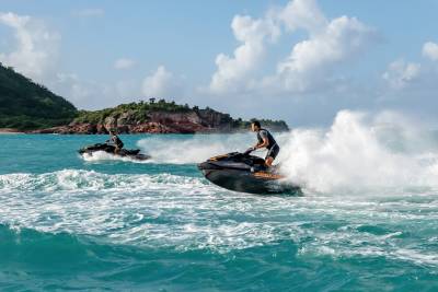 Two people race jet skis through turquoise waters with a lush green island in the background.