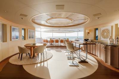 Sunlight streams into a luxurious yacht's dining and bar area, offering panoramic ocean views.