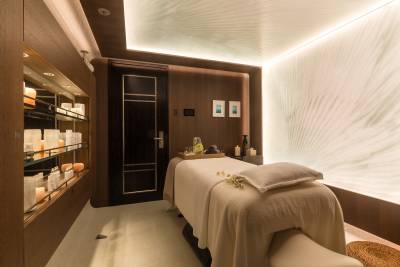 Experience ultimate relaxation in this serene spa room featuring a massage table, soothing lighting, and shelves stocked with luxurious spa products.