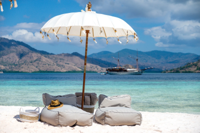 Relax on a pristine beach with comfortable seating and a traditional parasol overlooking a tranquil turquoise bay.