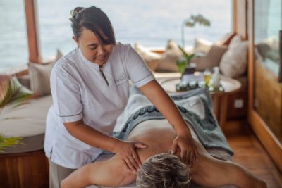 A masseuse provides a relaxing back massage to a client on a boat with ocean views.